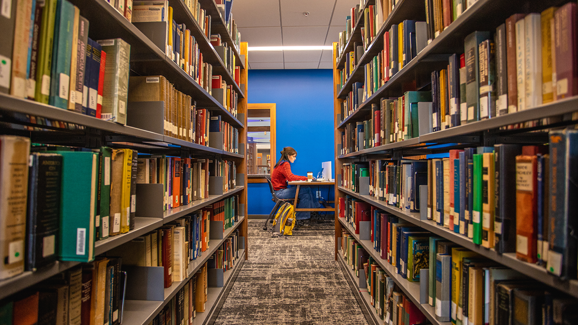 A student studying in the new library with books in the foreground. 
